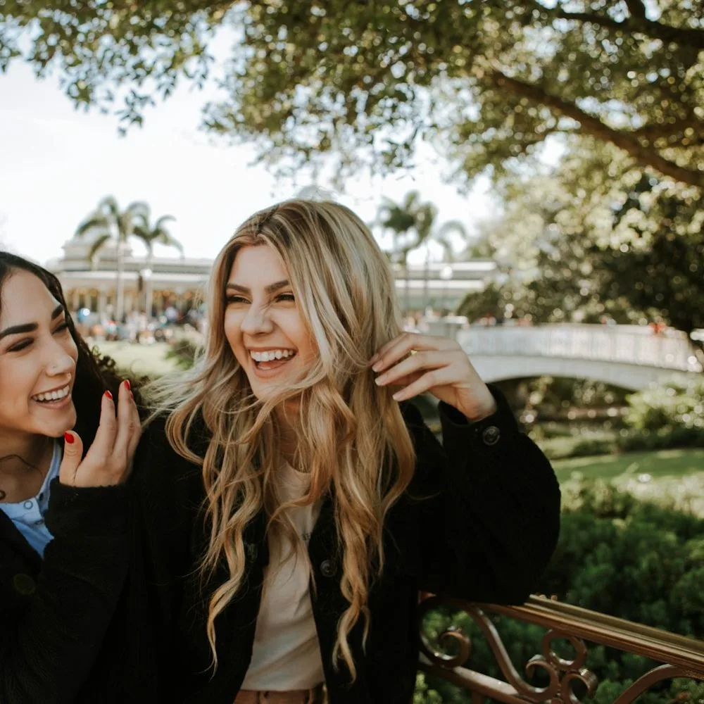 Two friends laughing together under trees on a bright day