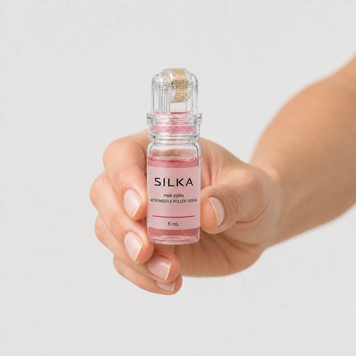 A hand holding the Silka Pink PDRN roller bottle, 5 ml, against a pale ground